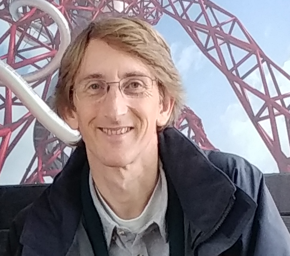 Man wearing glasses smiling at camera infront of rollercoaster